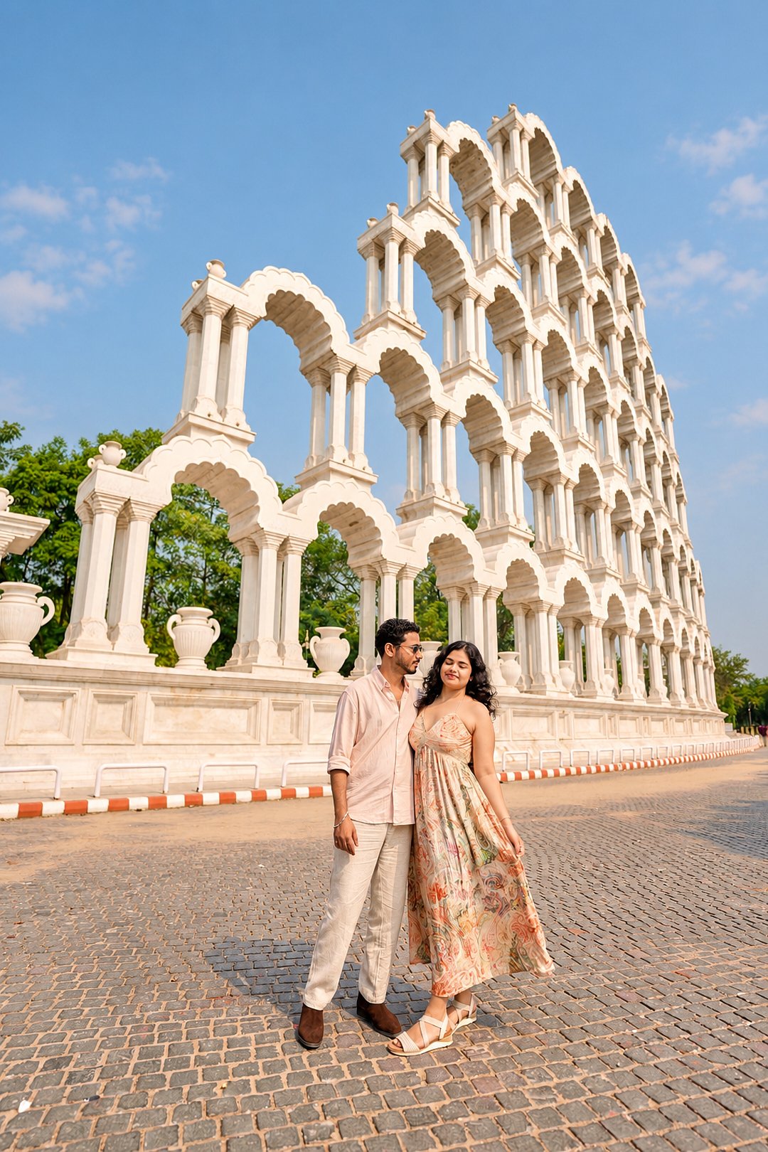 Cinematic pre-wedding film poster style photography of a couple running near grand white architecture at Jaipur Toran Dwar by Viresh Studio. sunny day
