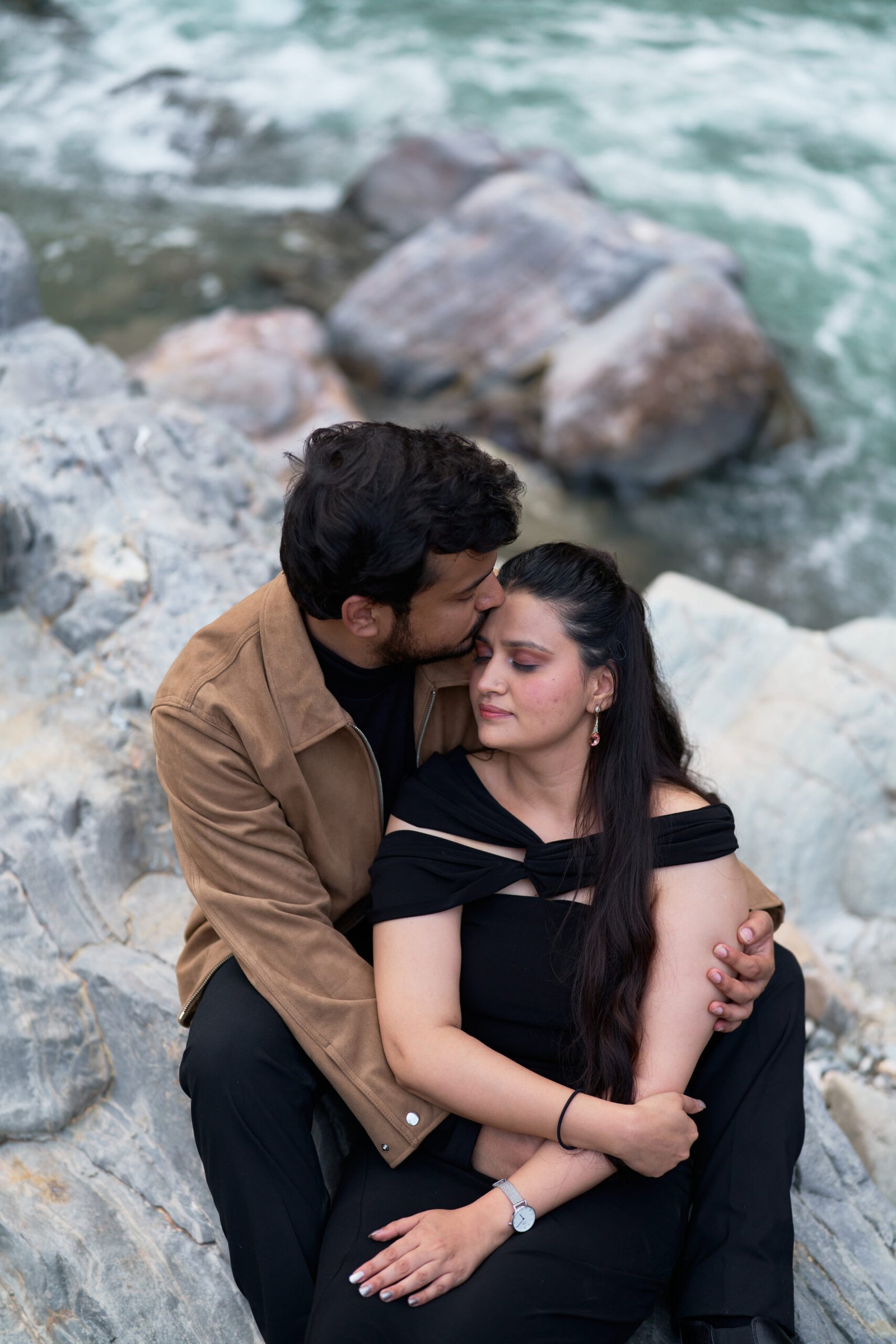 Couple standing by the river with a suspension bridge in the background during pre-wedding shoot