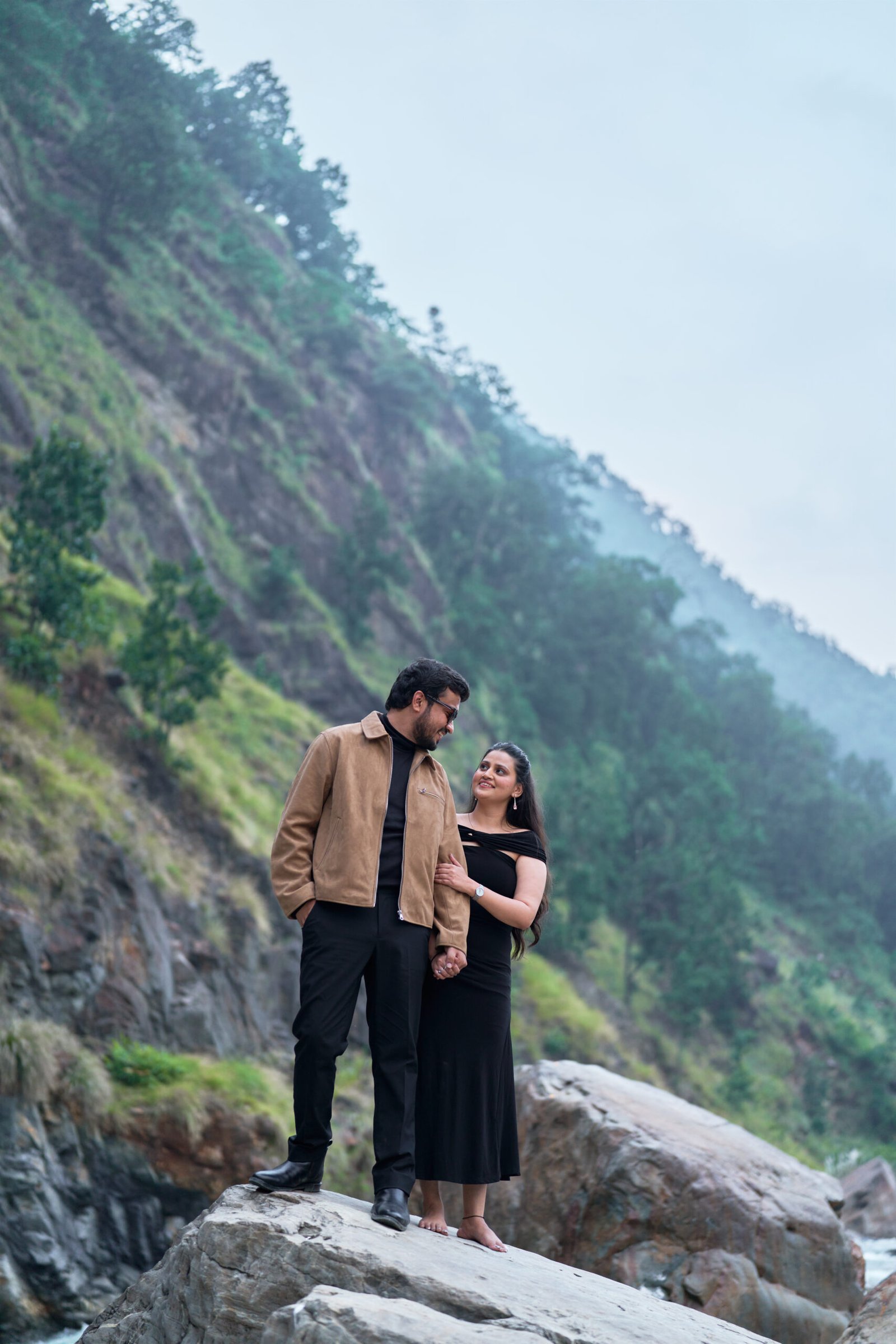 Couple standing by the river with a suspension bridge in the background during pre-wedding shoot