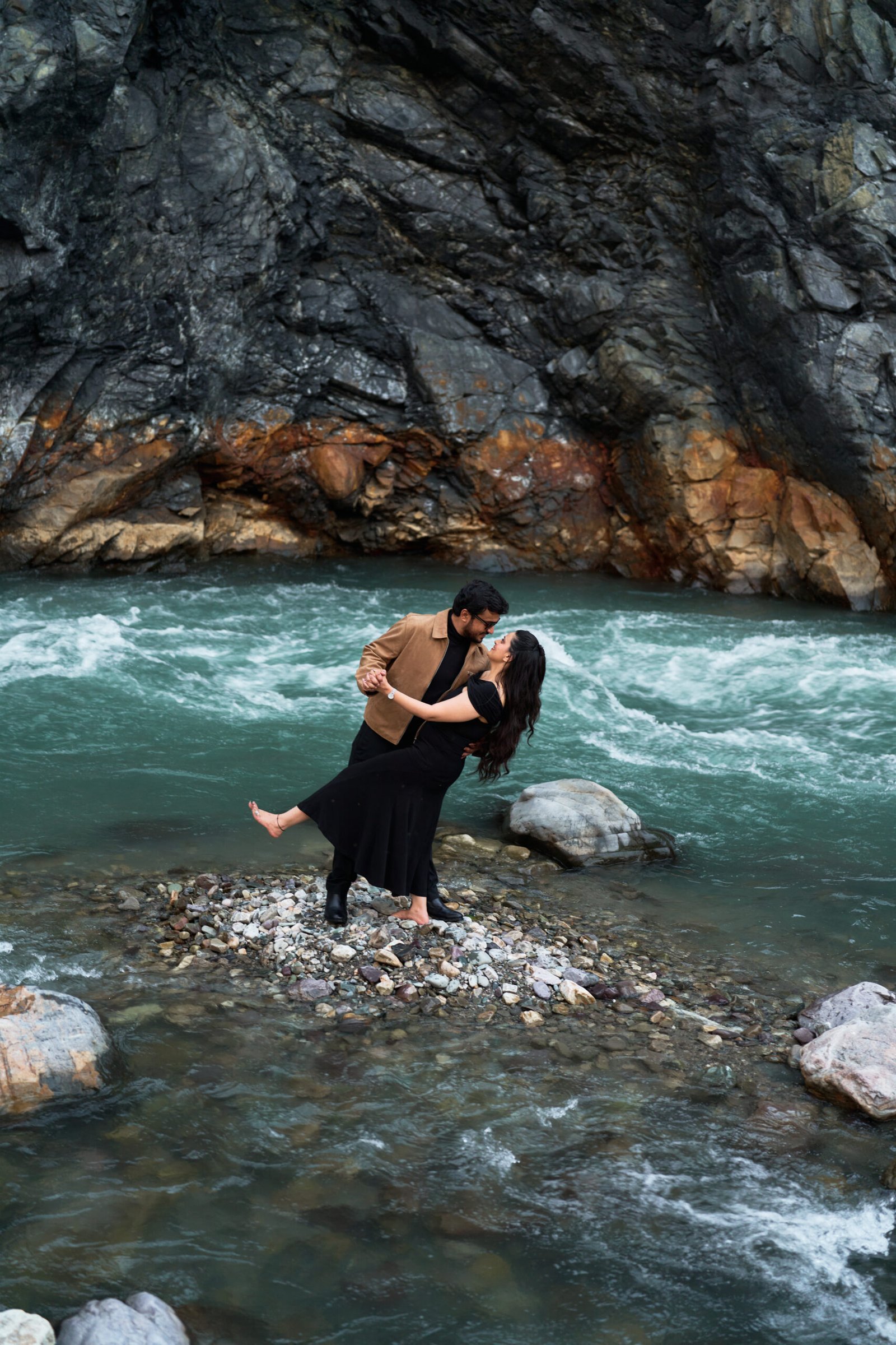 Couple standing by the river with a suspension bridge in the background during pre-wedding shoot